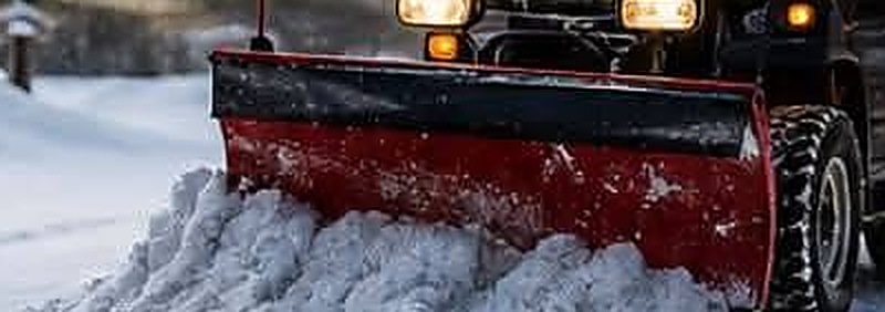 Truck with a plow blade clearing snow from a driveway